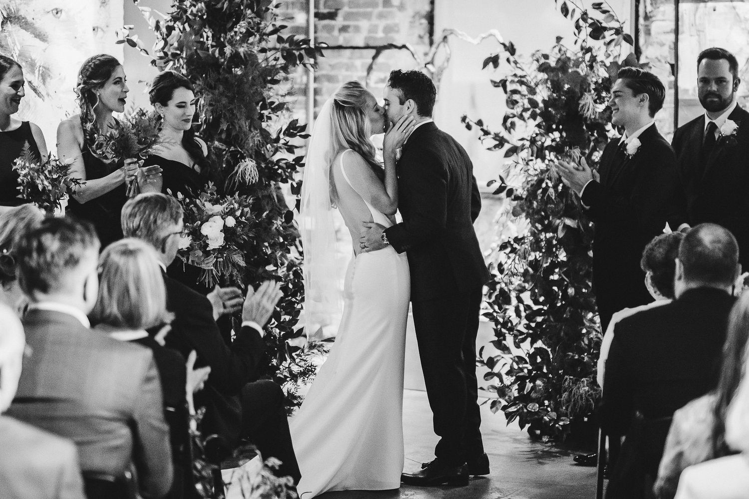 Black and white shot of wedding ceremony with floral arch decorations.
