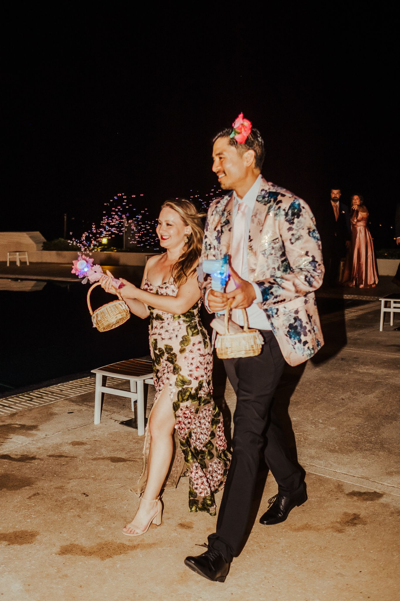 A couple in floral attire holding light-up party favors at a nighttime celebration.