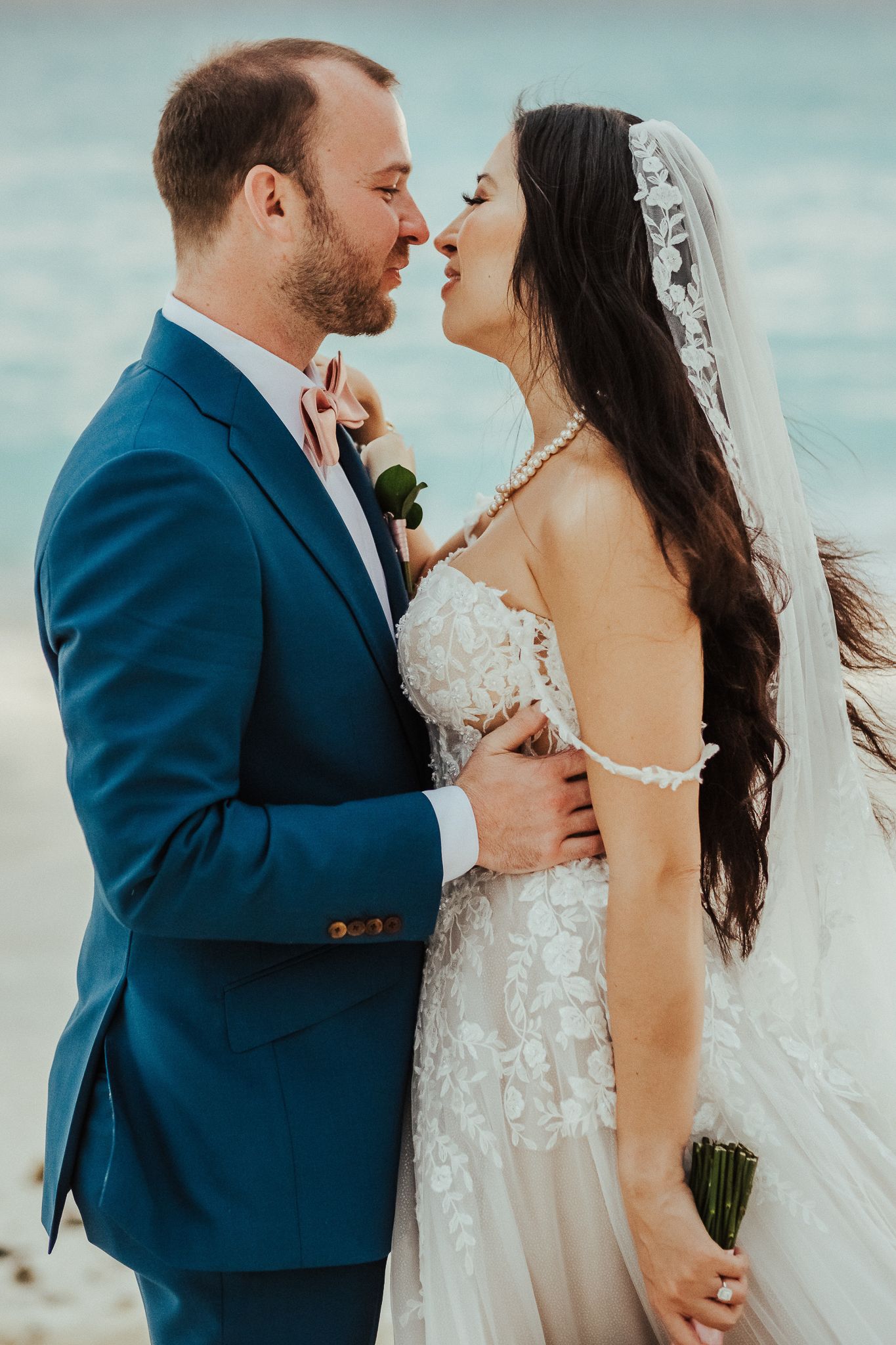 A candid beach wedding portrait of a couple sharing an intimate moment against turquoise waters.