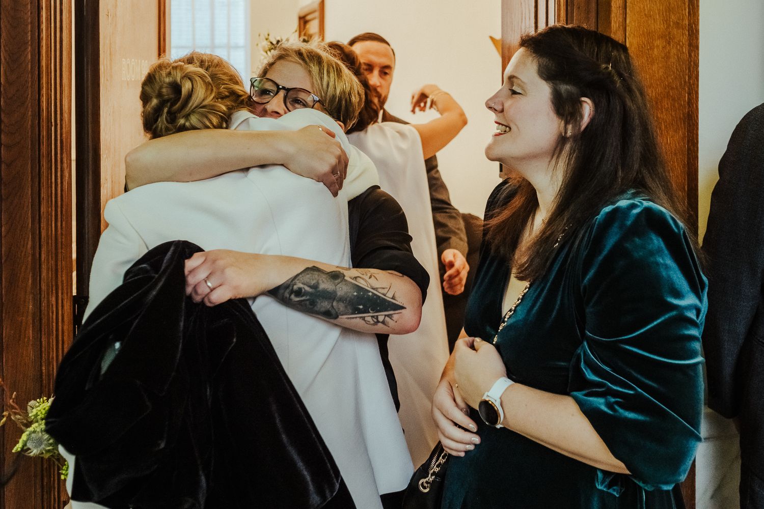Wedding guests celebrate with joyful hugs and laughter in an intimate indoor setting.
