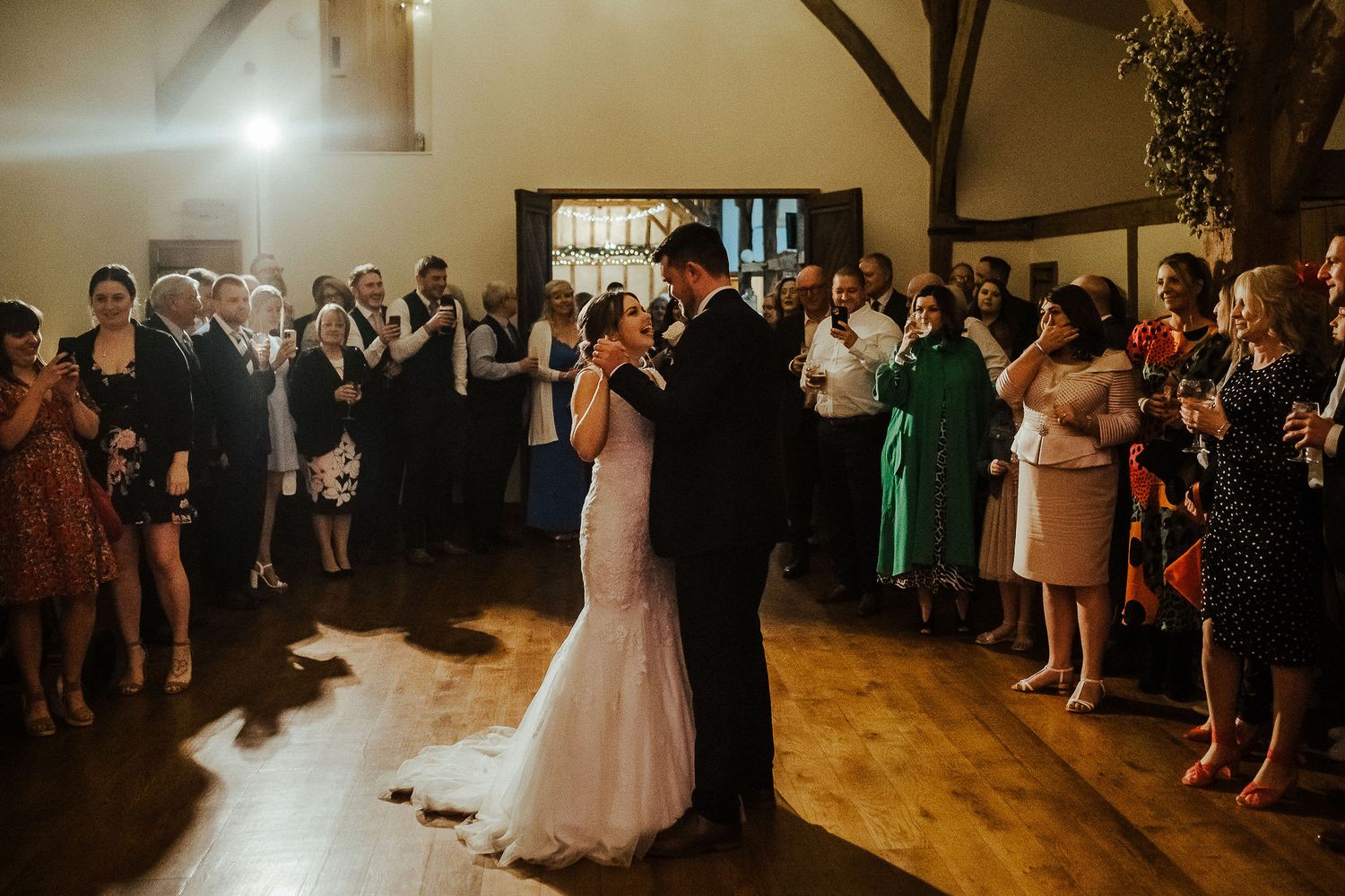 Wedding guests form a circle around the dance floor as a couple shares their first dance under warm lighting.