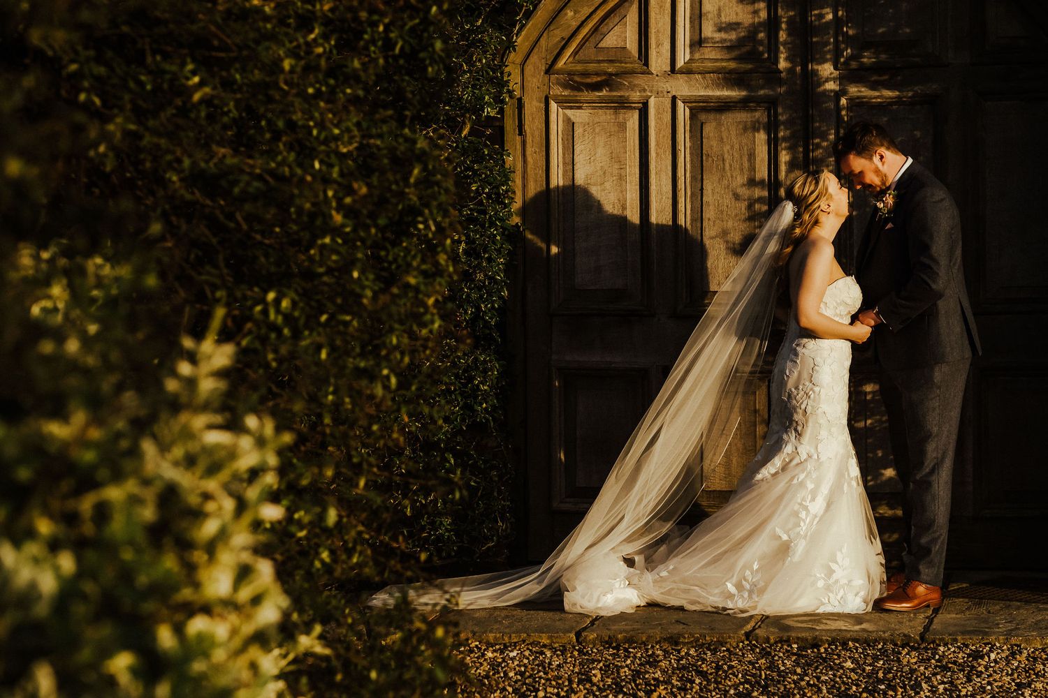 Romantic silhouette of couple in bridal attire against a rustic doorway at sunset.
