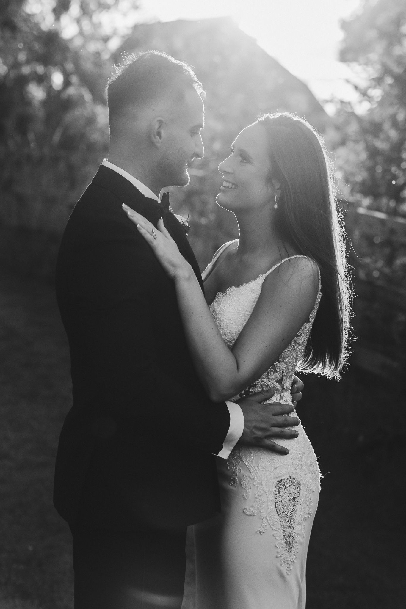 Black and white romantic portrait of newlyweds embracing in sunset lighting.