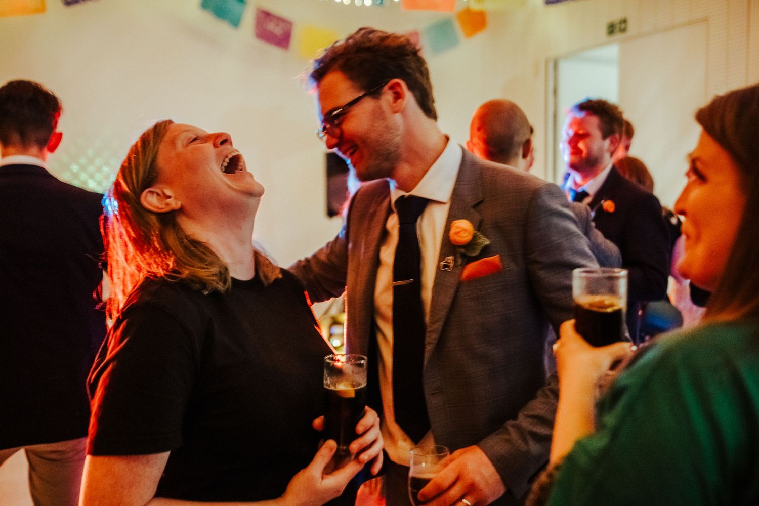Guests share joyful laughter at a festive indoor party with colorful decorations.