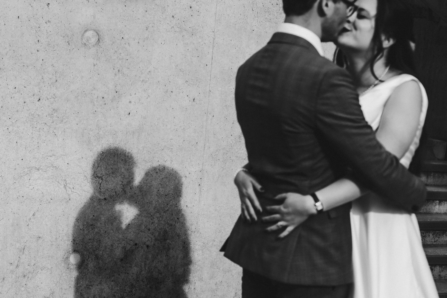 Silhouetted couple embracing against concrete wall in black and white.