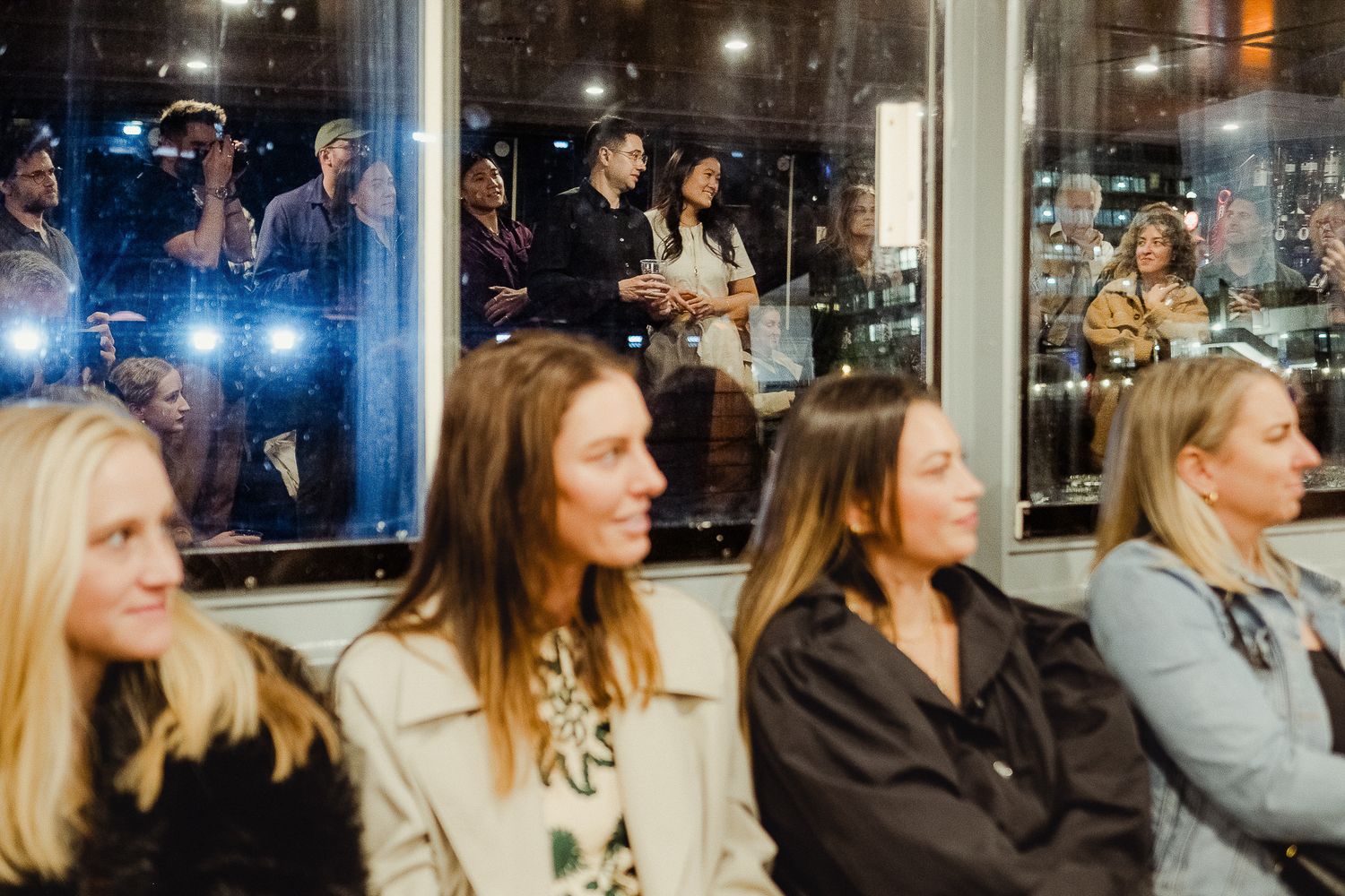 Diverse group of people seated in a restaurant at night looking attentively in one direction.