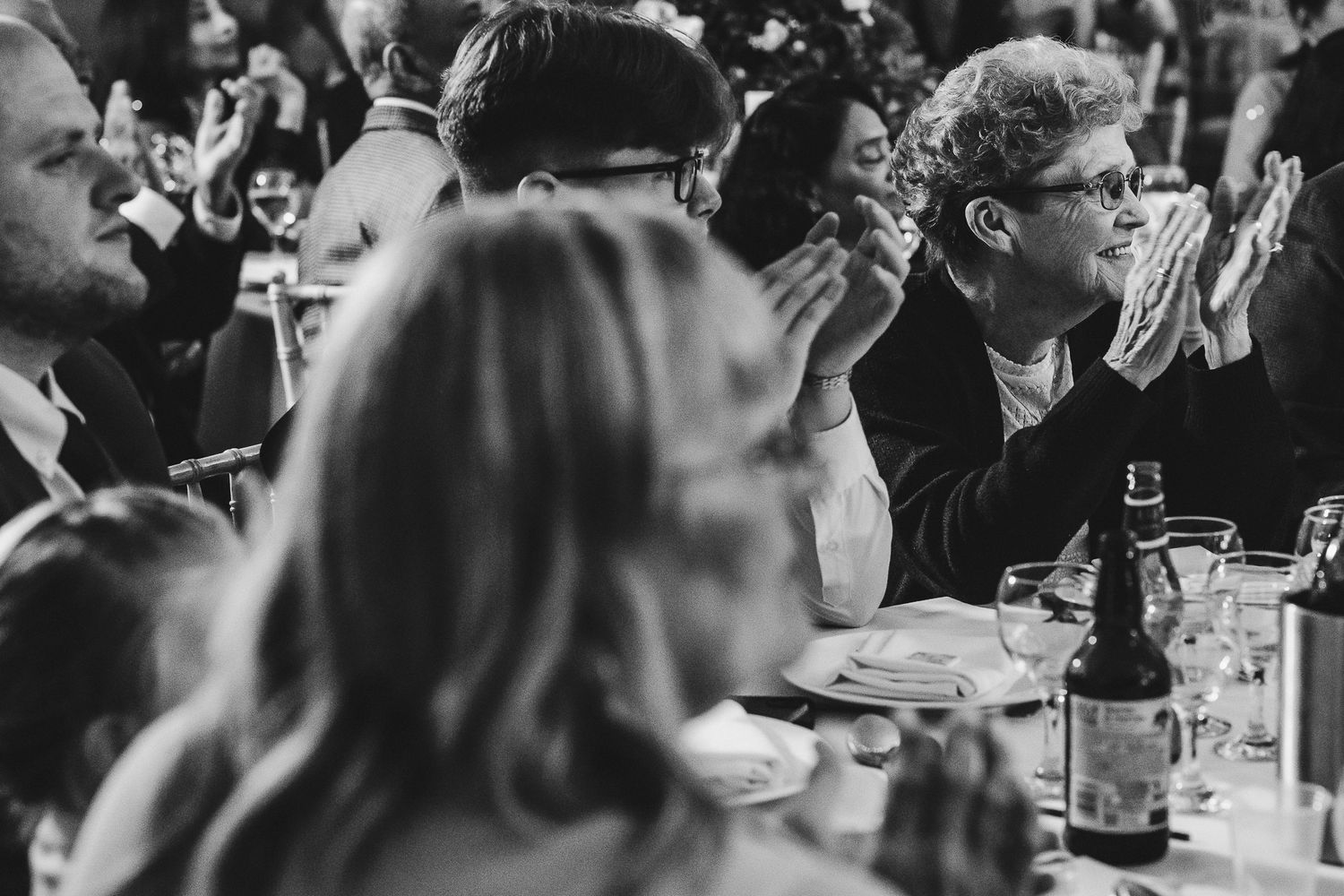 Black and white photo of guests clapping during a formal seated dinner event.