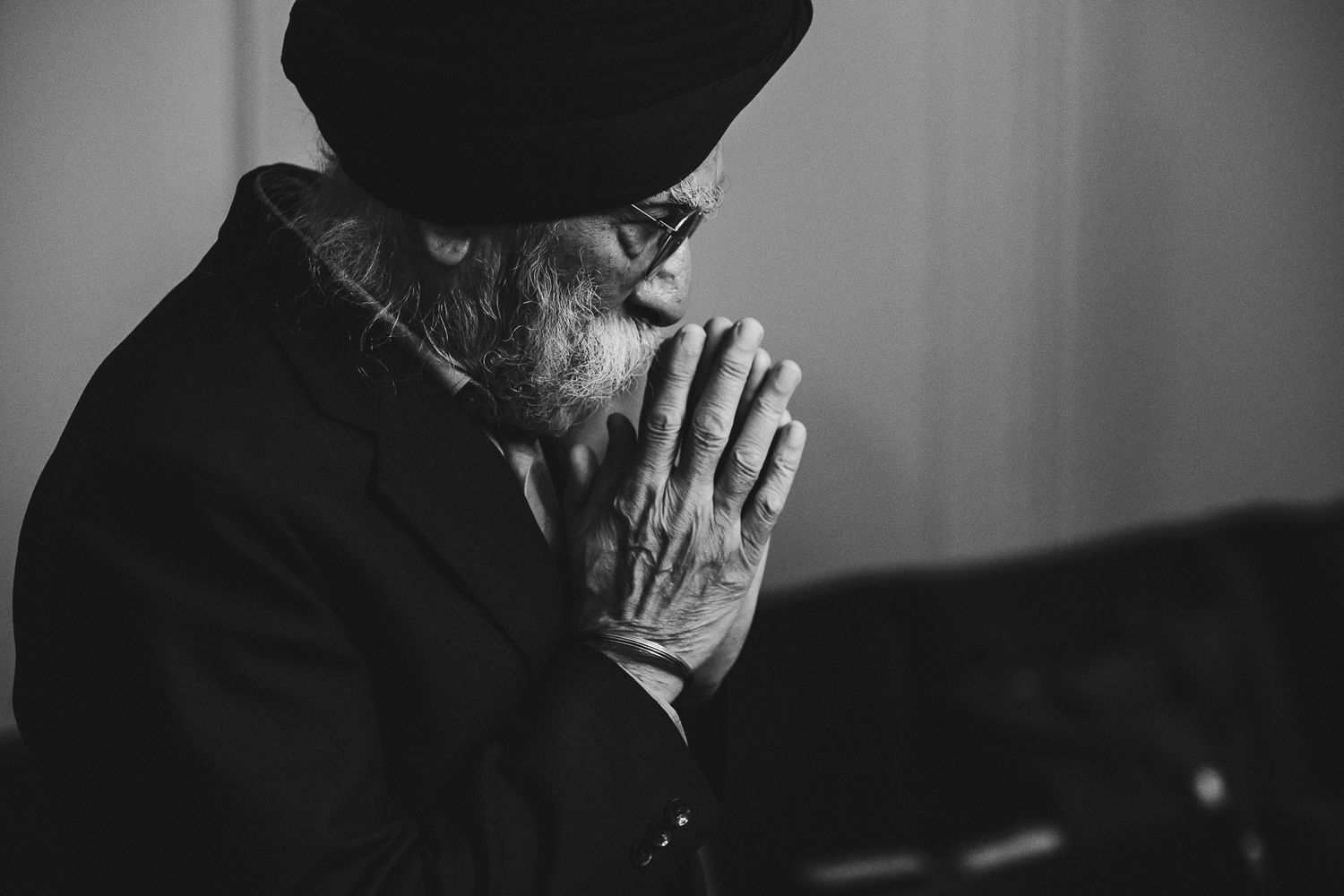 Black and white portrait of an elderly person in deep contemplation with clasped hands.