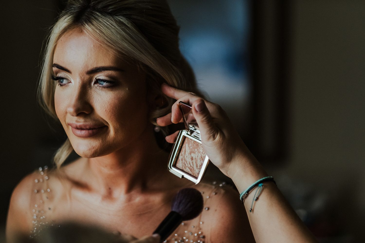 Bride putting on perfume in romantic window light during wedding preparations.