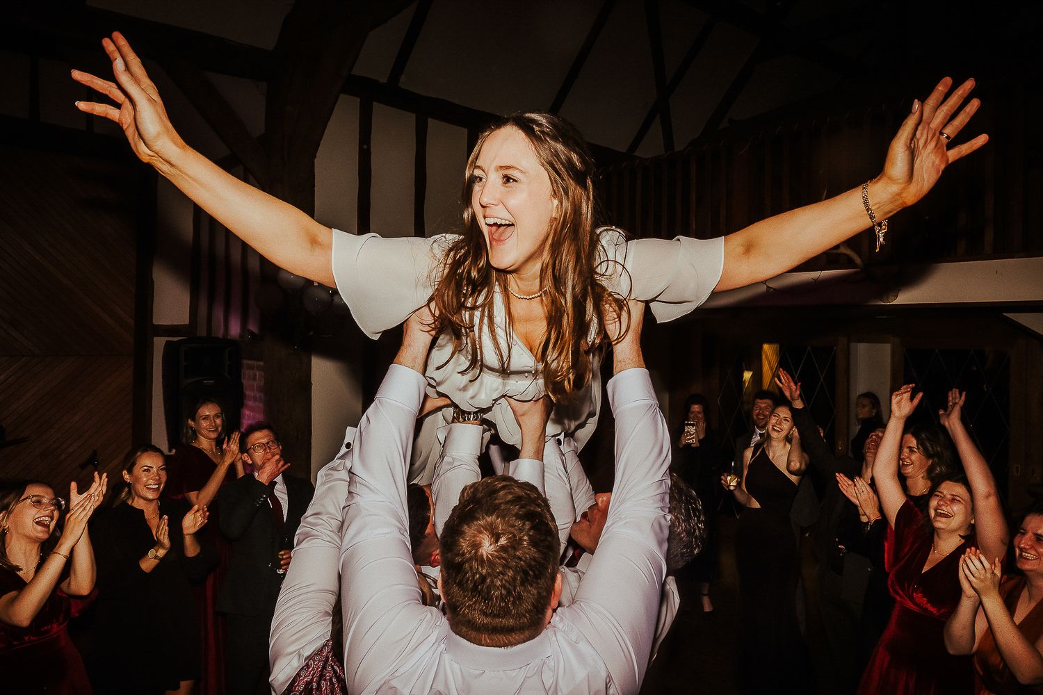Bride lifted high above crowd during joyous wedding reception dance.