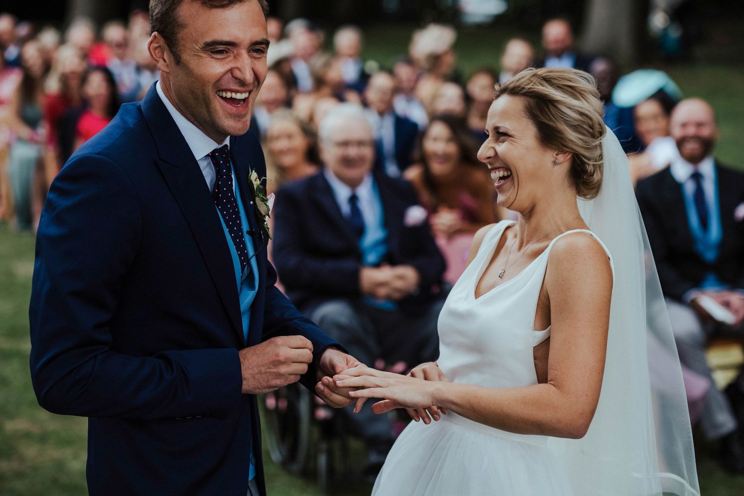 A couple exchange rings during an outdoor wedding ceremony surrounded by smiling guests.