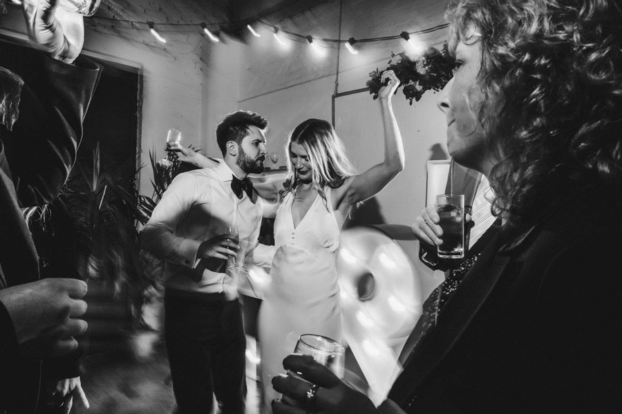 Reception guests dancing energetically together under decorative string lights at a celebratory evening event.
