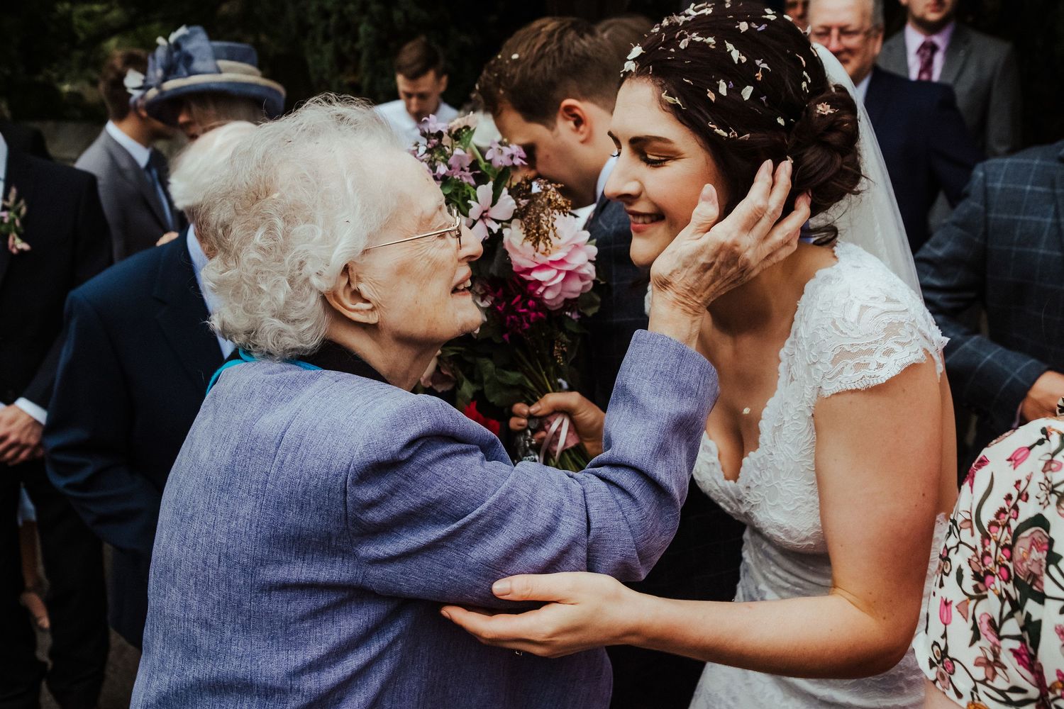 Emotional wedding moment between a bride and elderly woman during outdoor celebration.