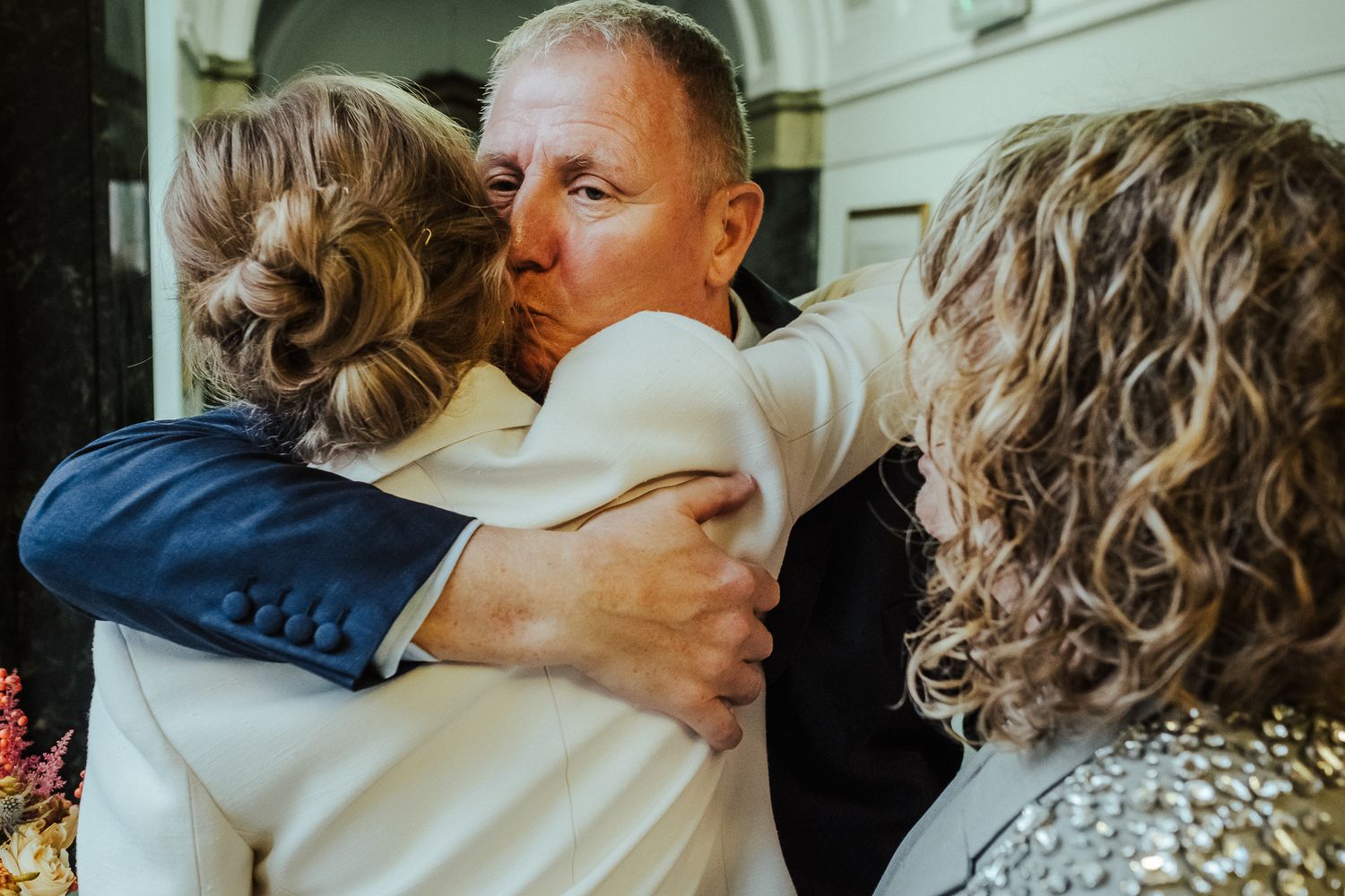 Emotional wedding moment showing embrace outside with someone in navy suit and white outfit.