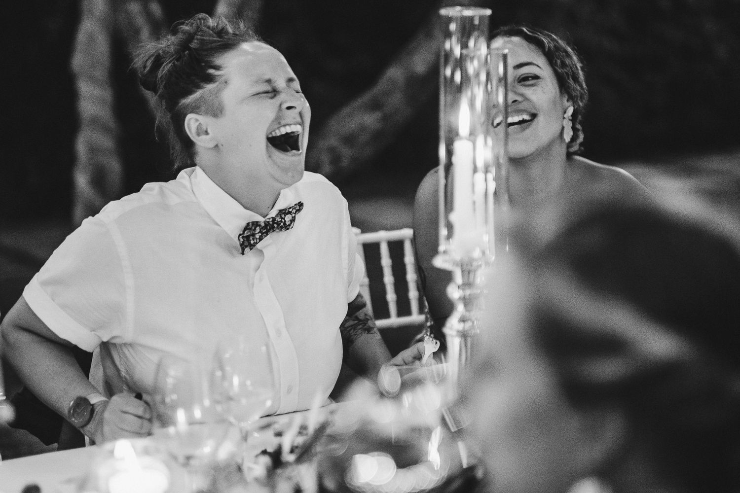 Black and white candid photo of guests laughing during outdoor dinner reception.
