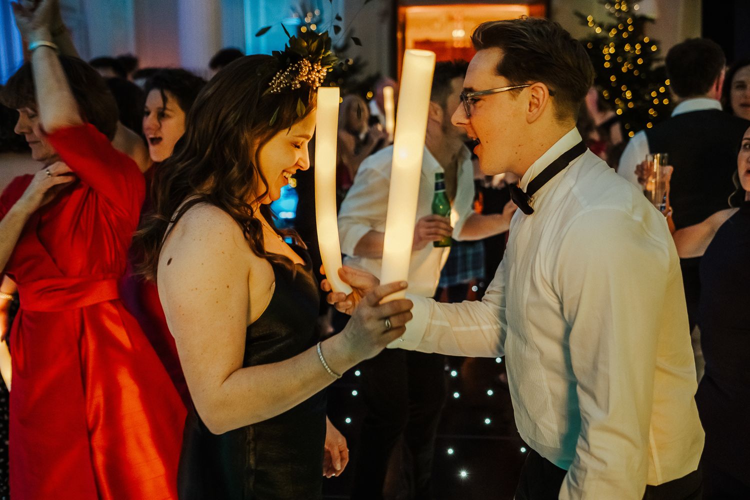 Wedding guests dancing and socializing under festive lighting with Christmas decorations visible.