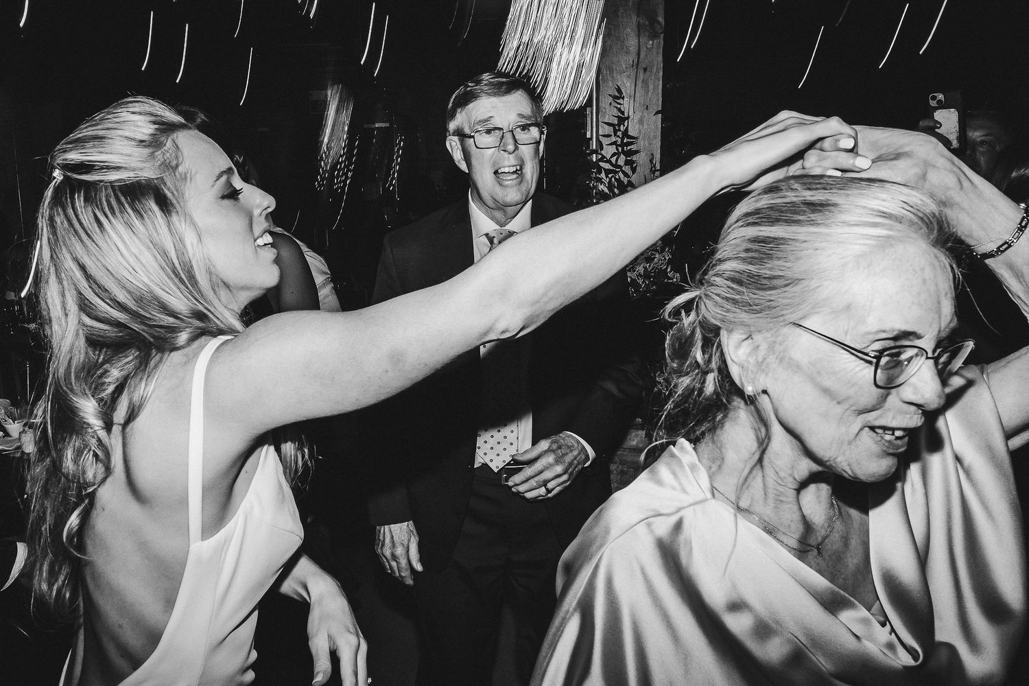 Party guests dance energetically on a crowded dance floor at a wedding reception.