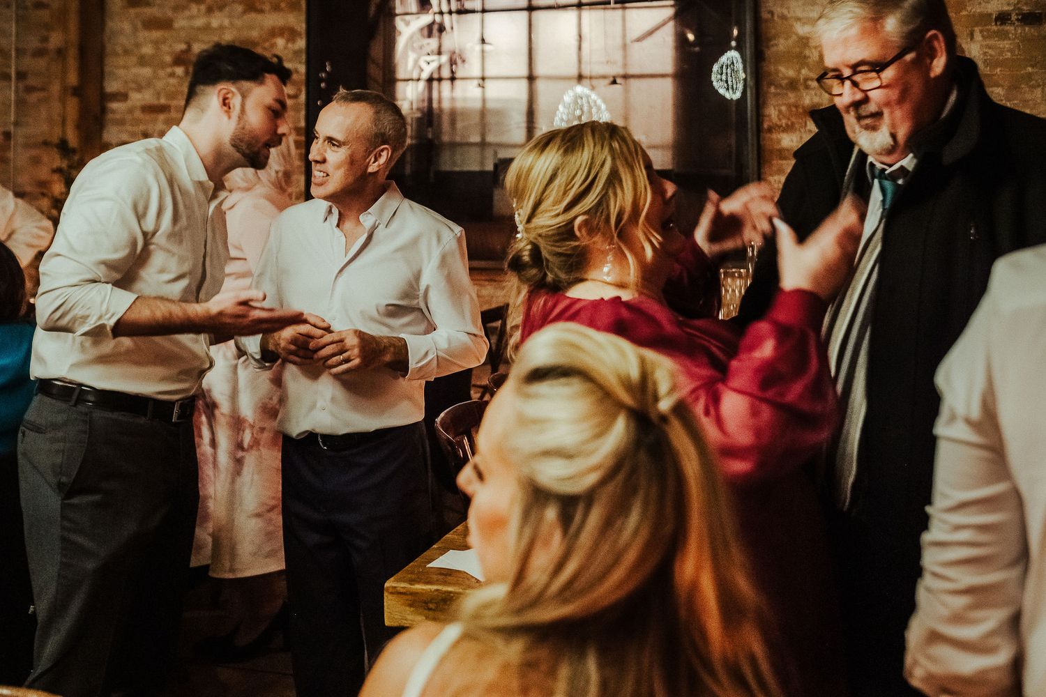 Candid party scene in a rustic venue with exposed brick walls and natural lighting.