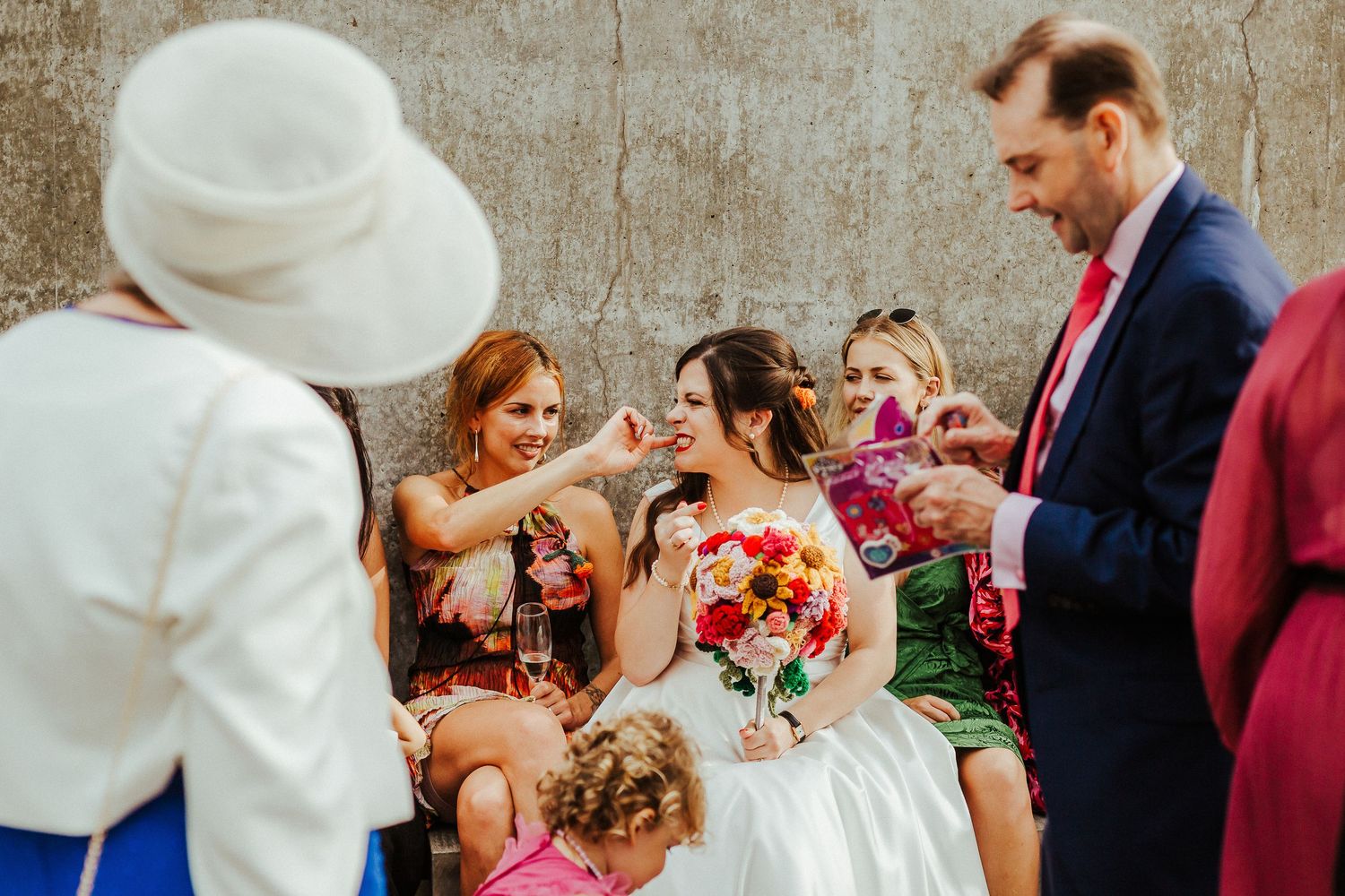 Wedding party celebrates with champagne outdoors against a concrete wall.