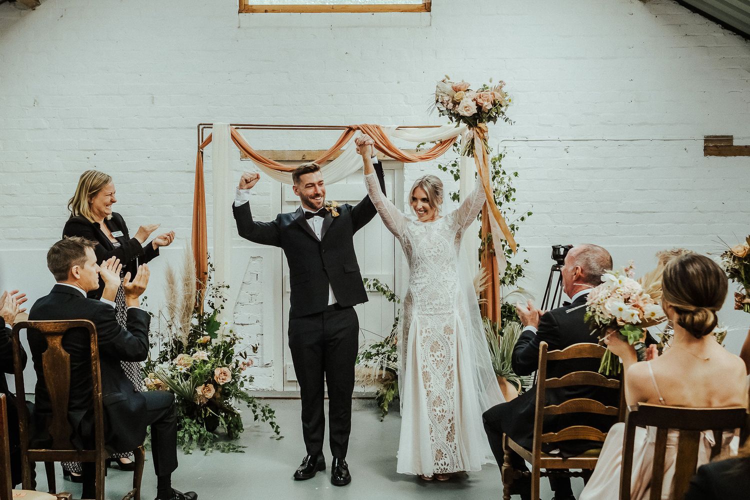 Wedding ceremony in white modern venue with floral arch and minimalist decor.
