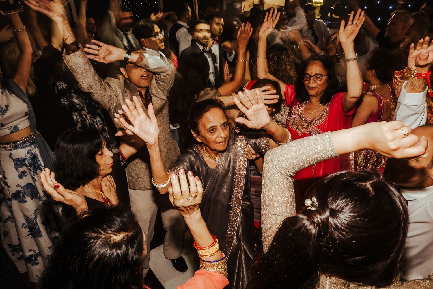 Energetic crowd of wedding guests dancing and raising their hands on a packed dance floor during reception celebration.