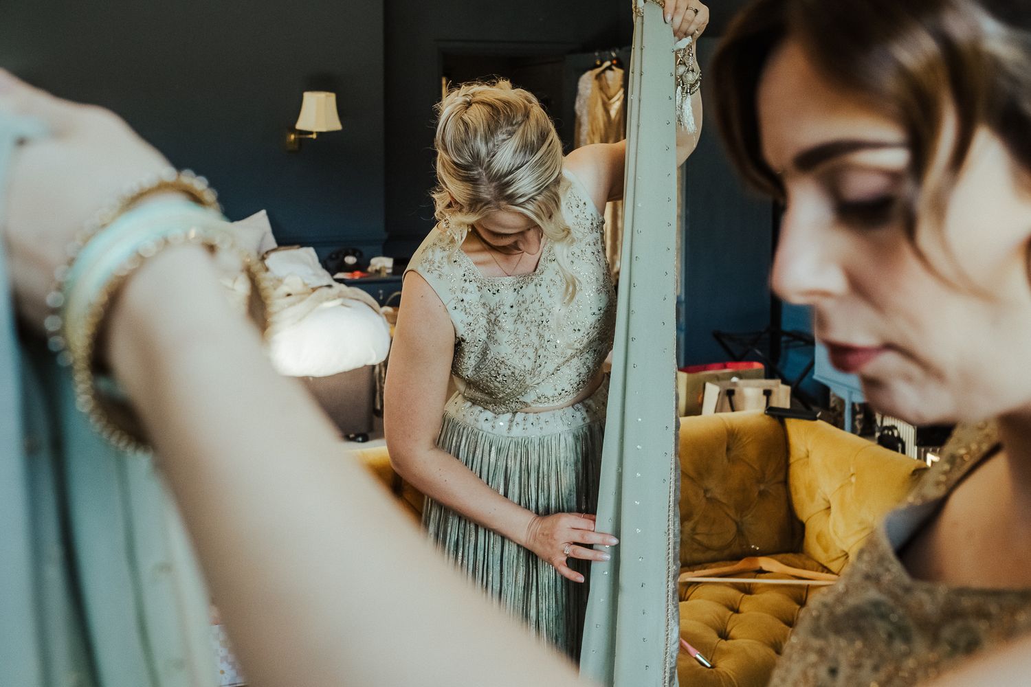 A group of people in formal attire preparing in a blue-walled room with elegant dresses and decorative details.