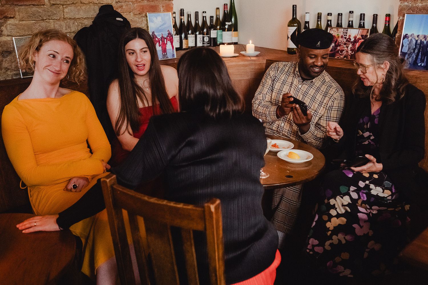 Group of friends sharing drinks and conversation at a cozy restaurant table with exposed brick wall.