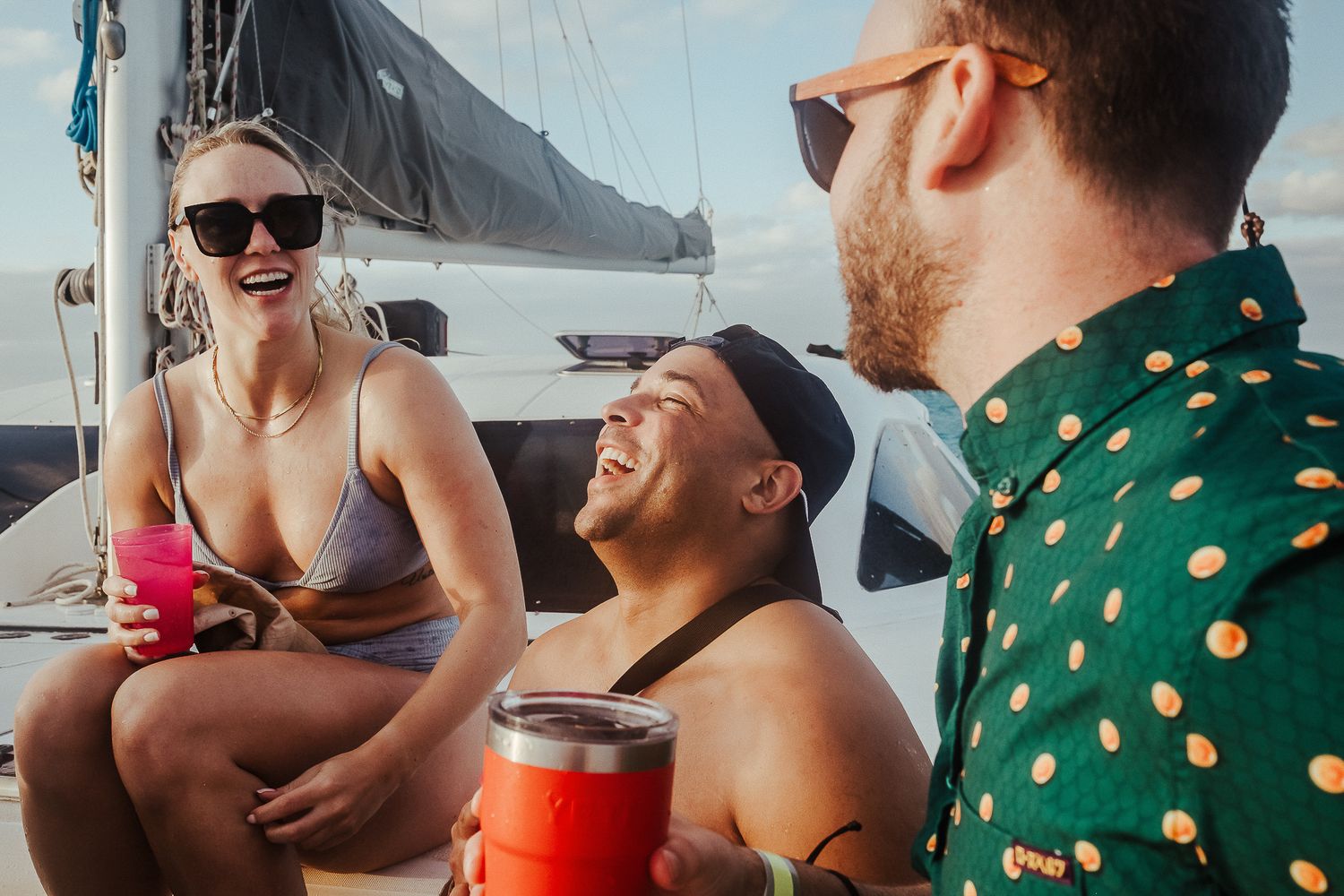 Three friends sharing drinks and laughter on a boat deck under sunny skies.