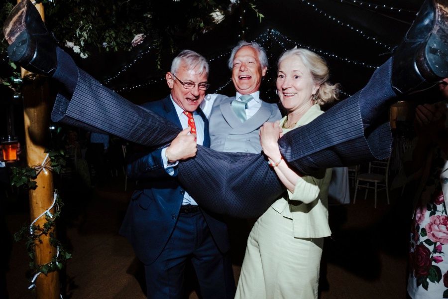 Three guests joyfully dancing together at an evening wedding celebration.