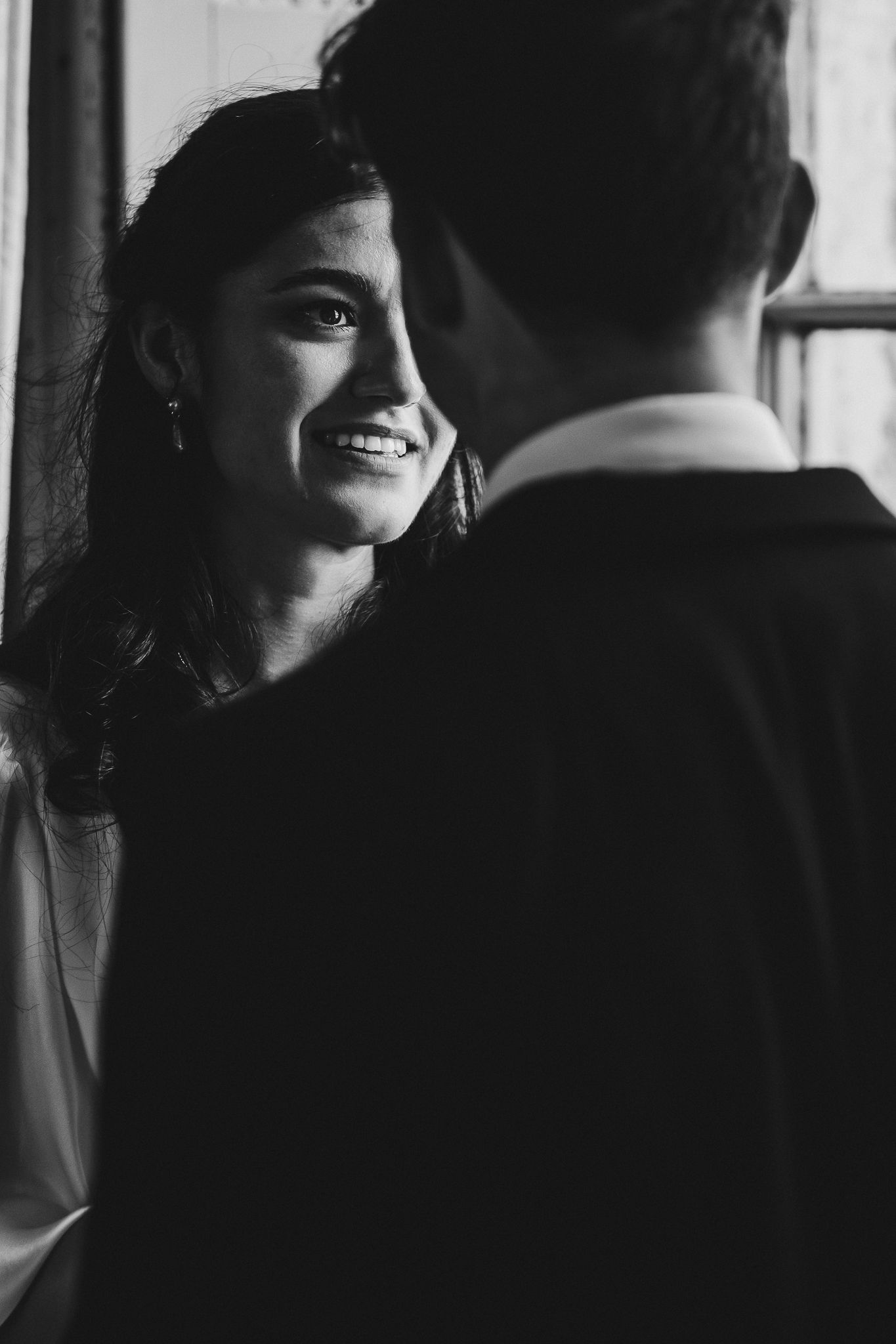 Black and white wedding portrait of couple by window sharing intimate moment.