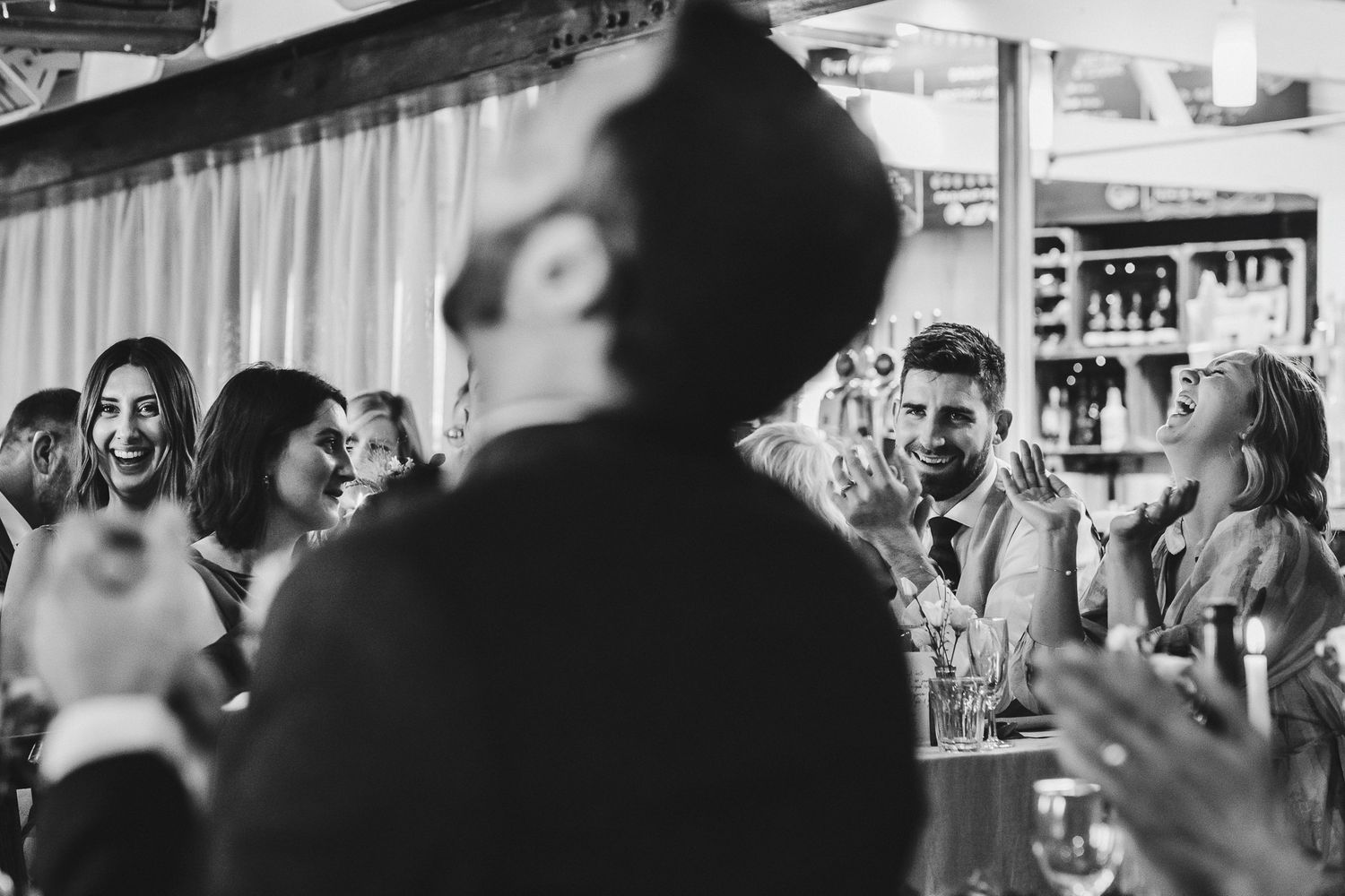 Black and white candid photo of wedding guests laughing during reception.