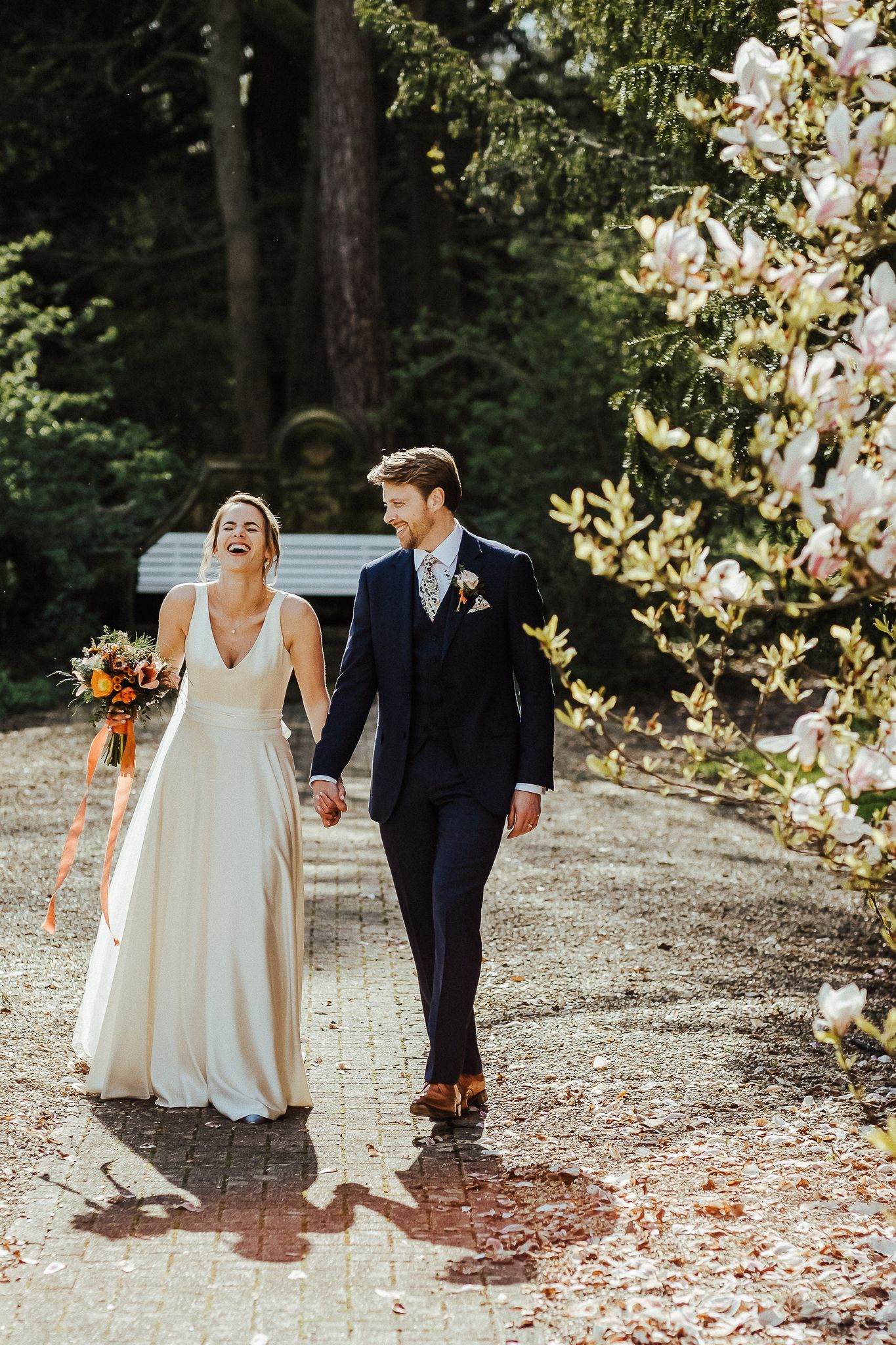 Couple walking hand in hand on garden path in elegant wedding attire.