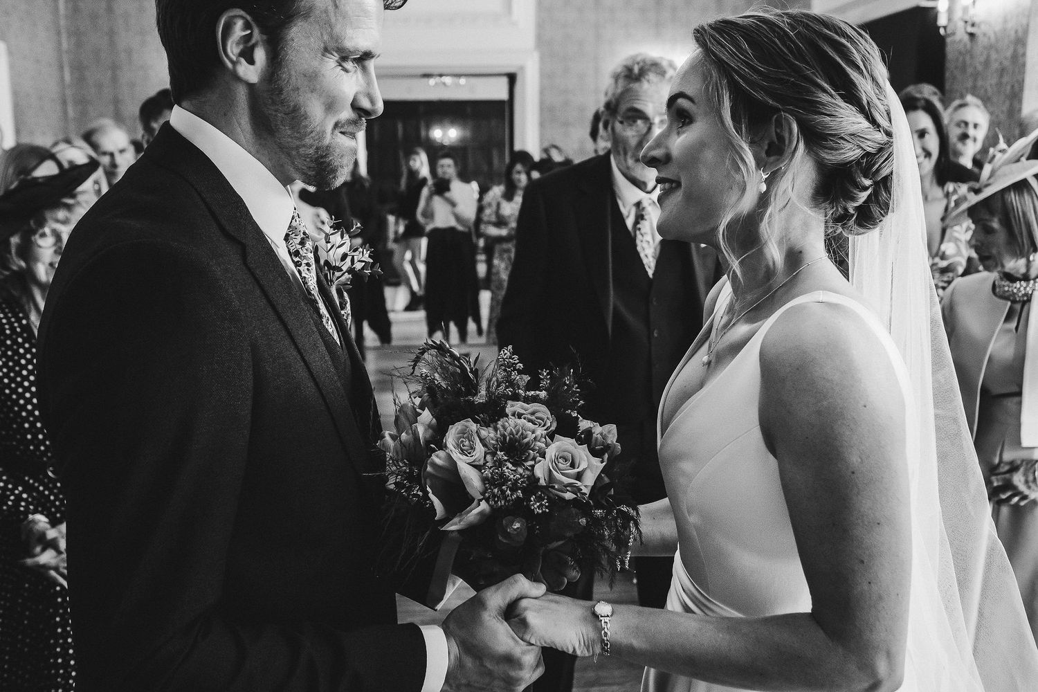 Black and white ceremony photo of couple exchanging rings at altar.