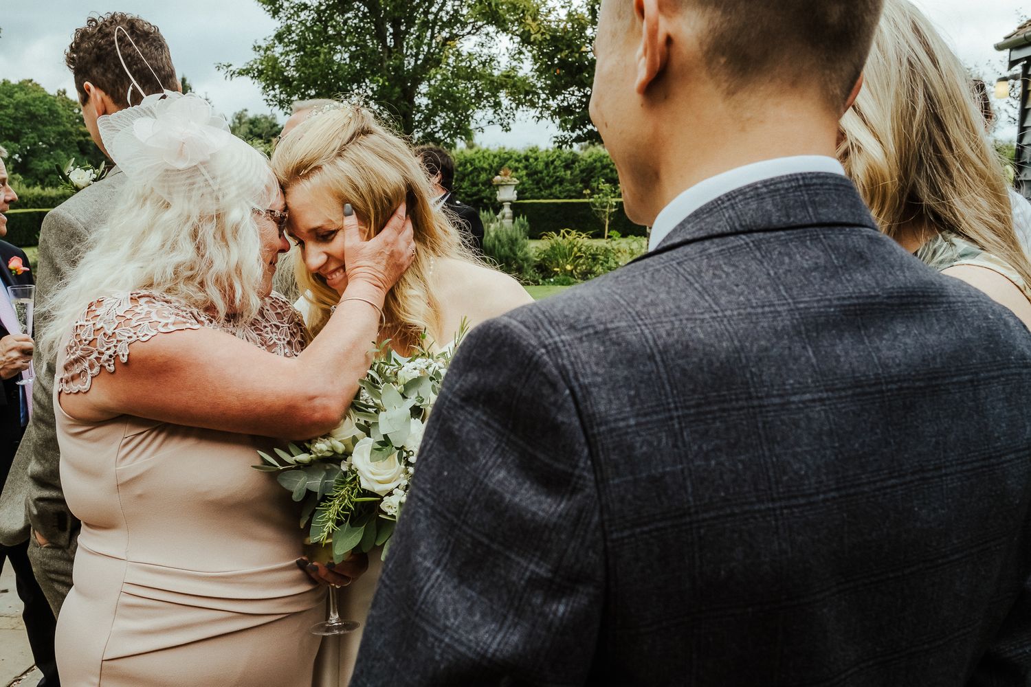 Wedding party gathering outdoors on a sunny day surrounded by lush greenery.