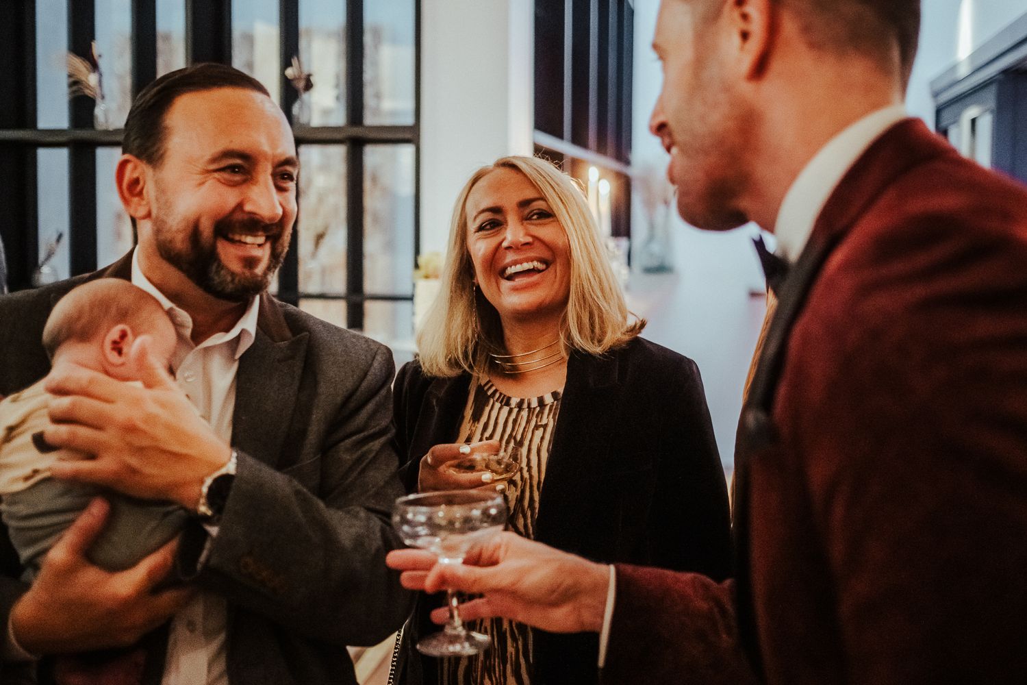 Three wedding guests share drinks and laughter at reception.