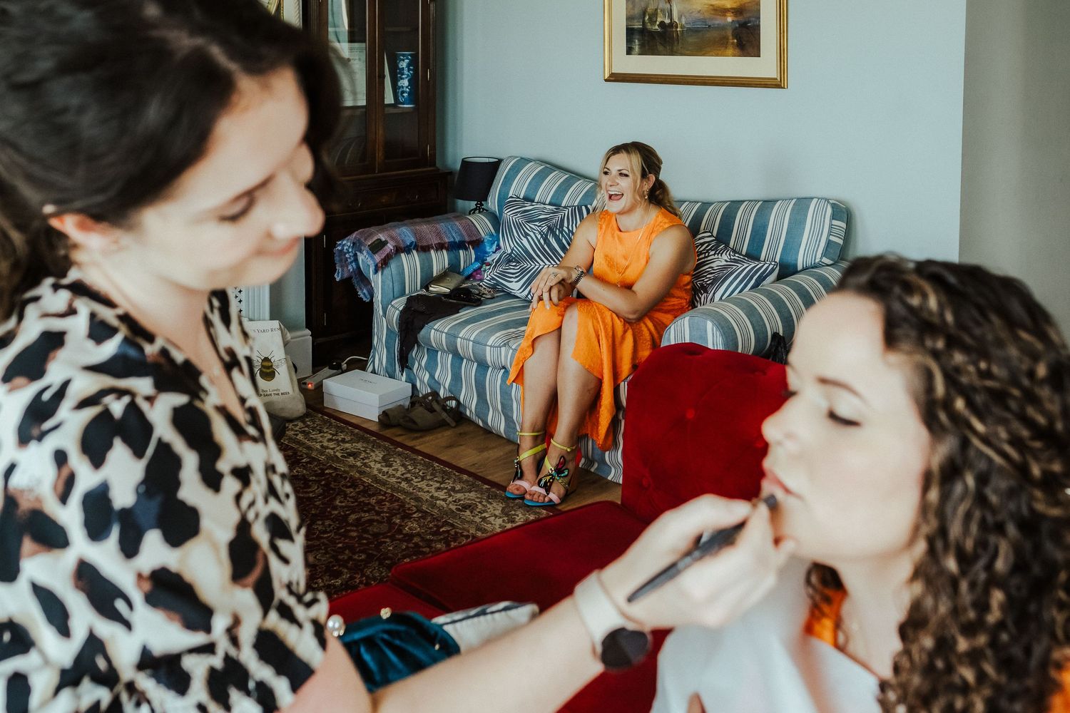 Wedding preparation scene with orange bridesmaids dress and makeup application in progress.