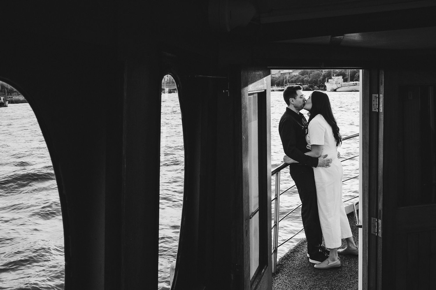 Black and white photo of two people silhouetted in a boat doorway with water visible.