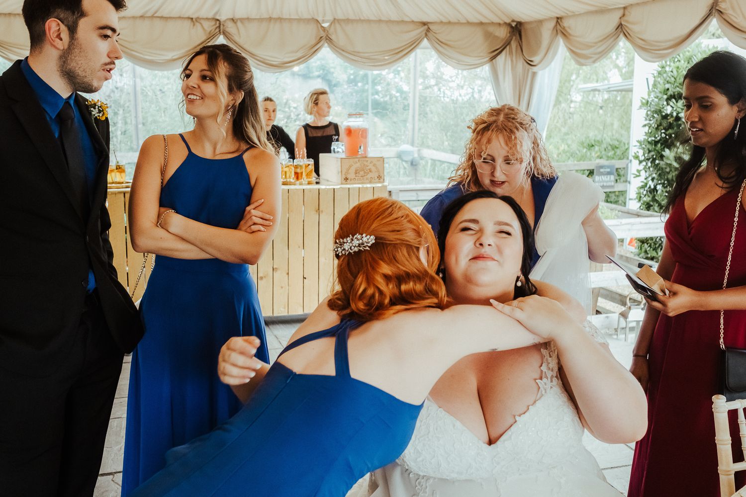 Wedding reception under a white tent with guests in colorful formal attire.