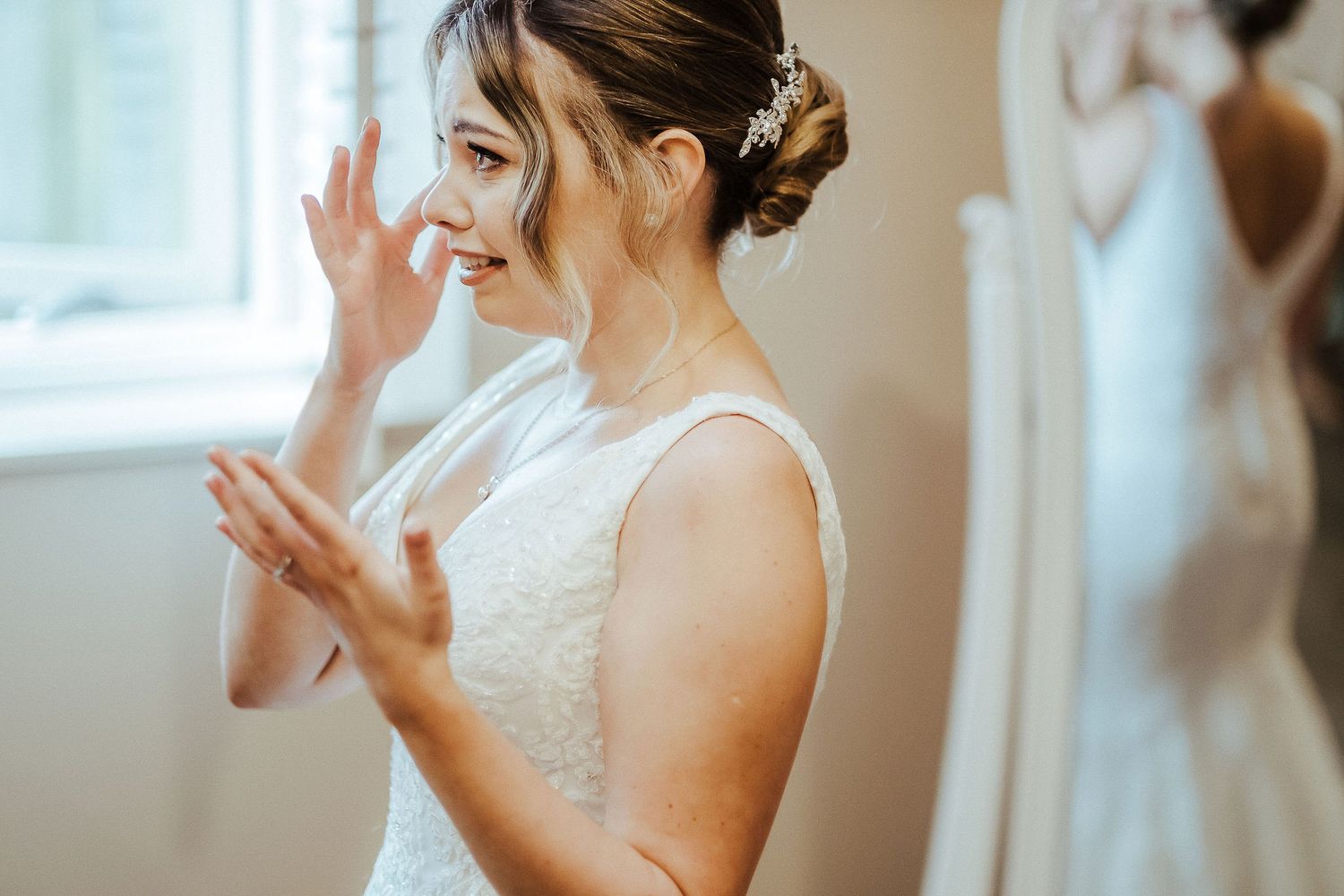 Bride in an elegant white dress adjusts her jewelry while getting ready.