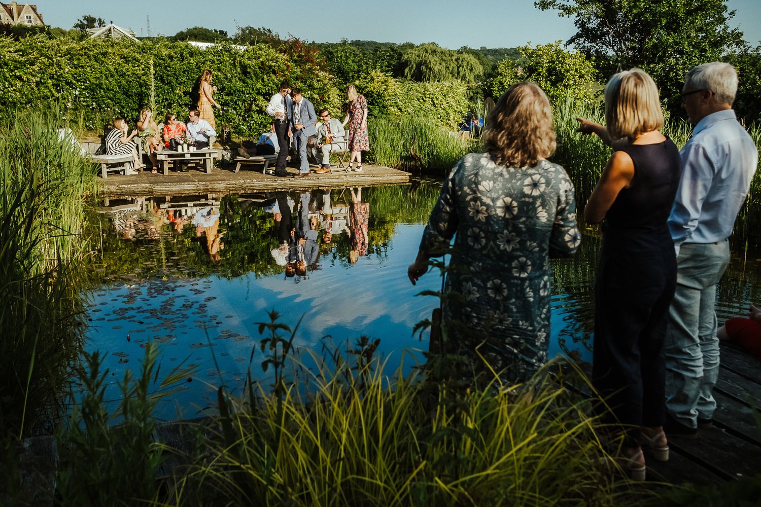 Wedding ceremony takes place in scenic outdoor garden setting near water.