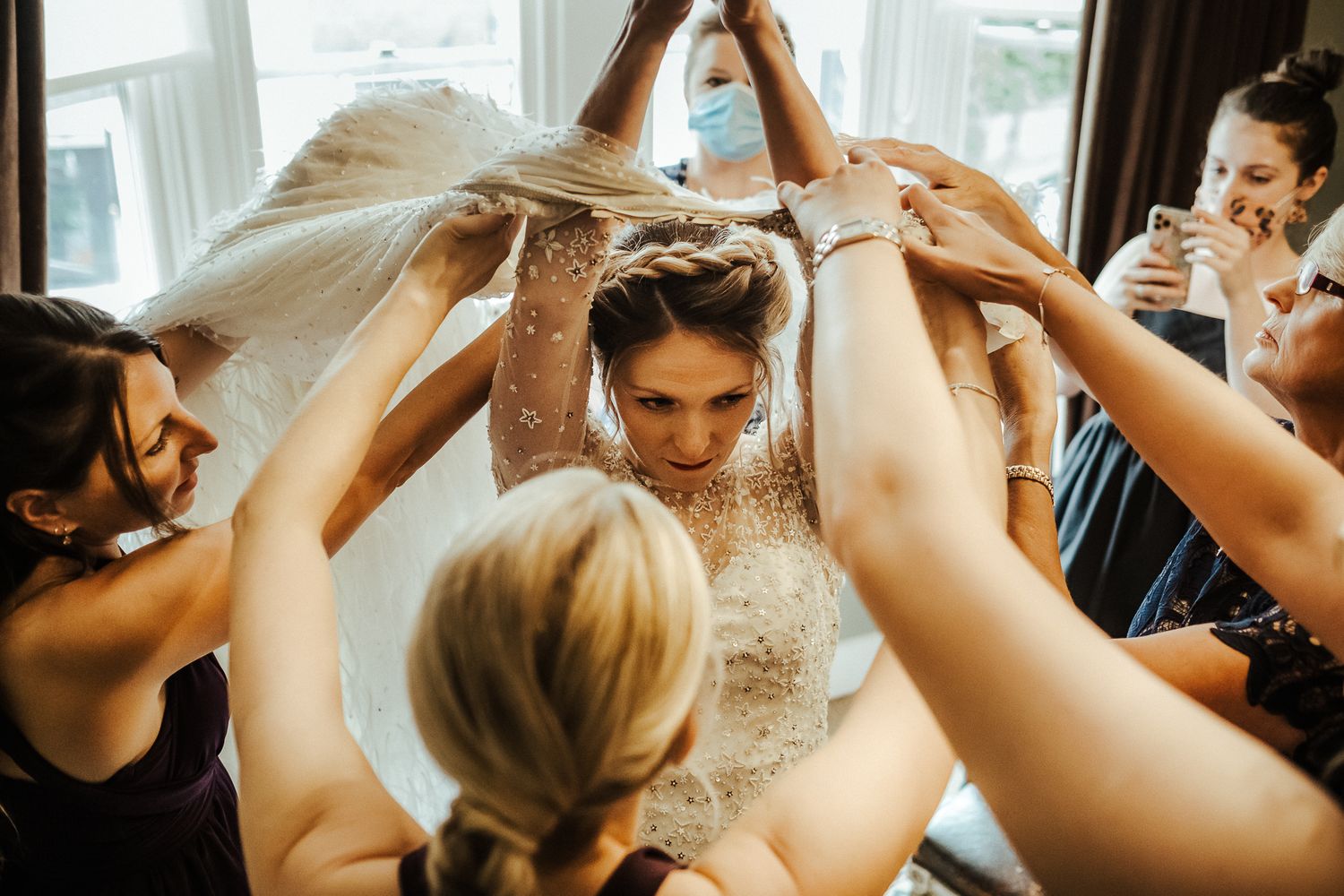 Wedding dress preparation scene with multiple hands helping the bride.