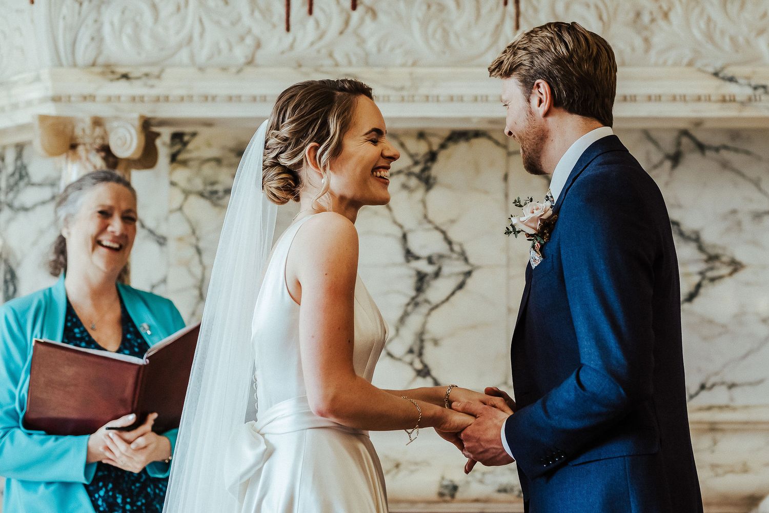 Wedding couple shares joyful moment during their ceremony with officiant in elegant marble room.
