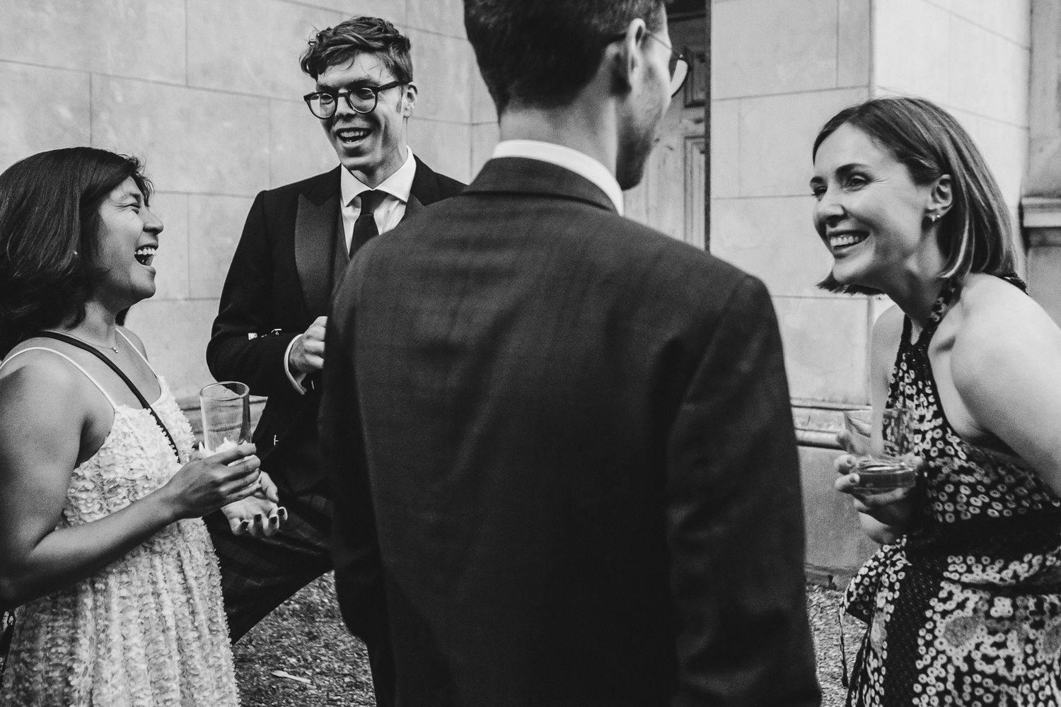 Black and white photo of guests engaged in lively conversation at an elegant social gathering.
