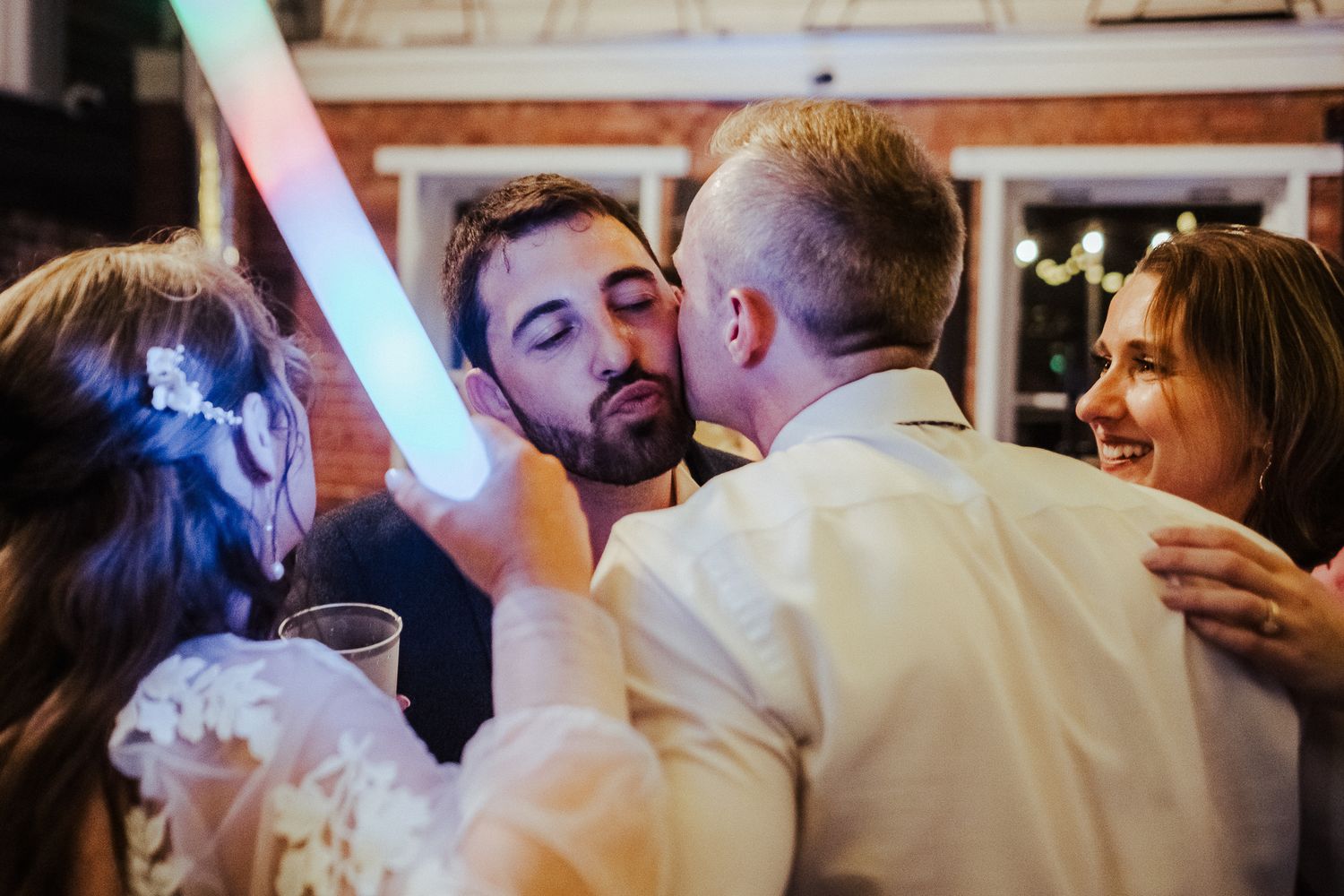 Wedding guests wave illuminated LED foam sticks while dancing at an indoor reception.