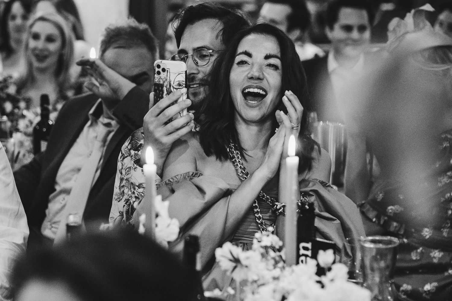 Guest laughs joyfully while capturing moments on their phone during a celebration.