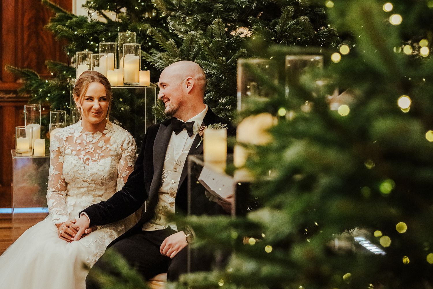 Romantic Christmas wedding portrait by decorated tree in elegant venue.