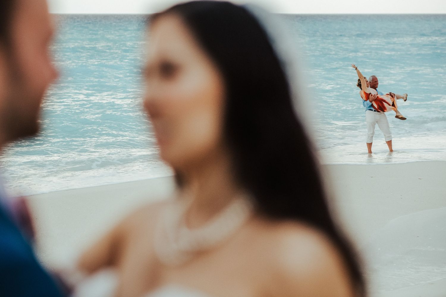 Creative beach wedding photo with background figures jumping while couple remains in focus.