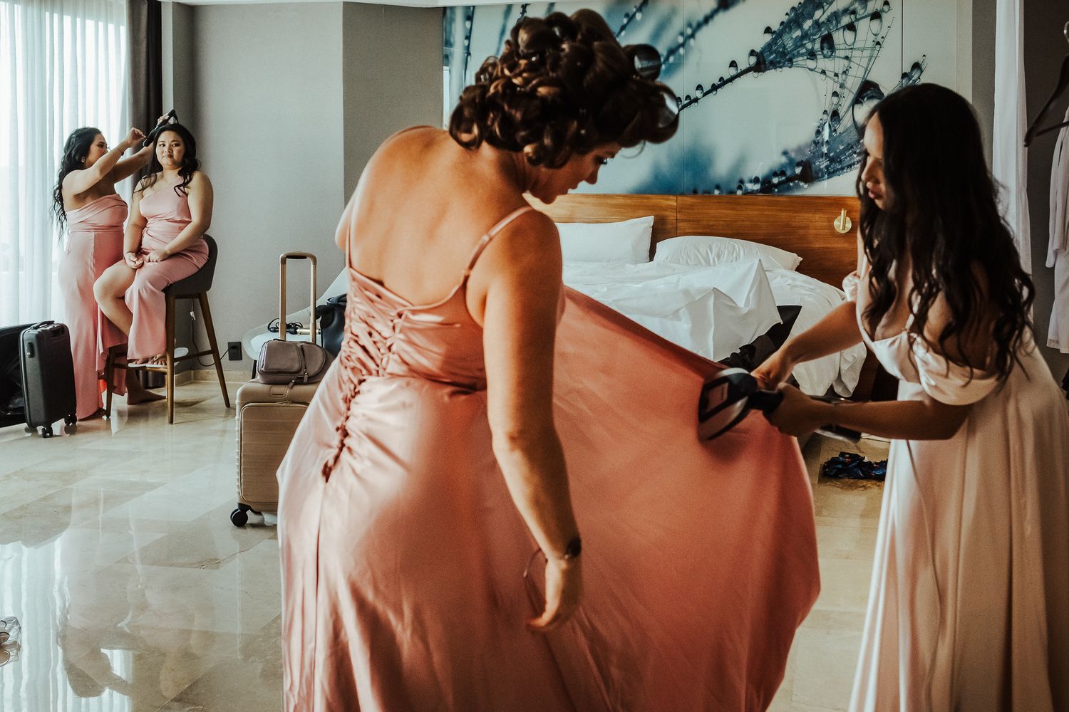 People helping adjust a flowing pink dress in a bright room.