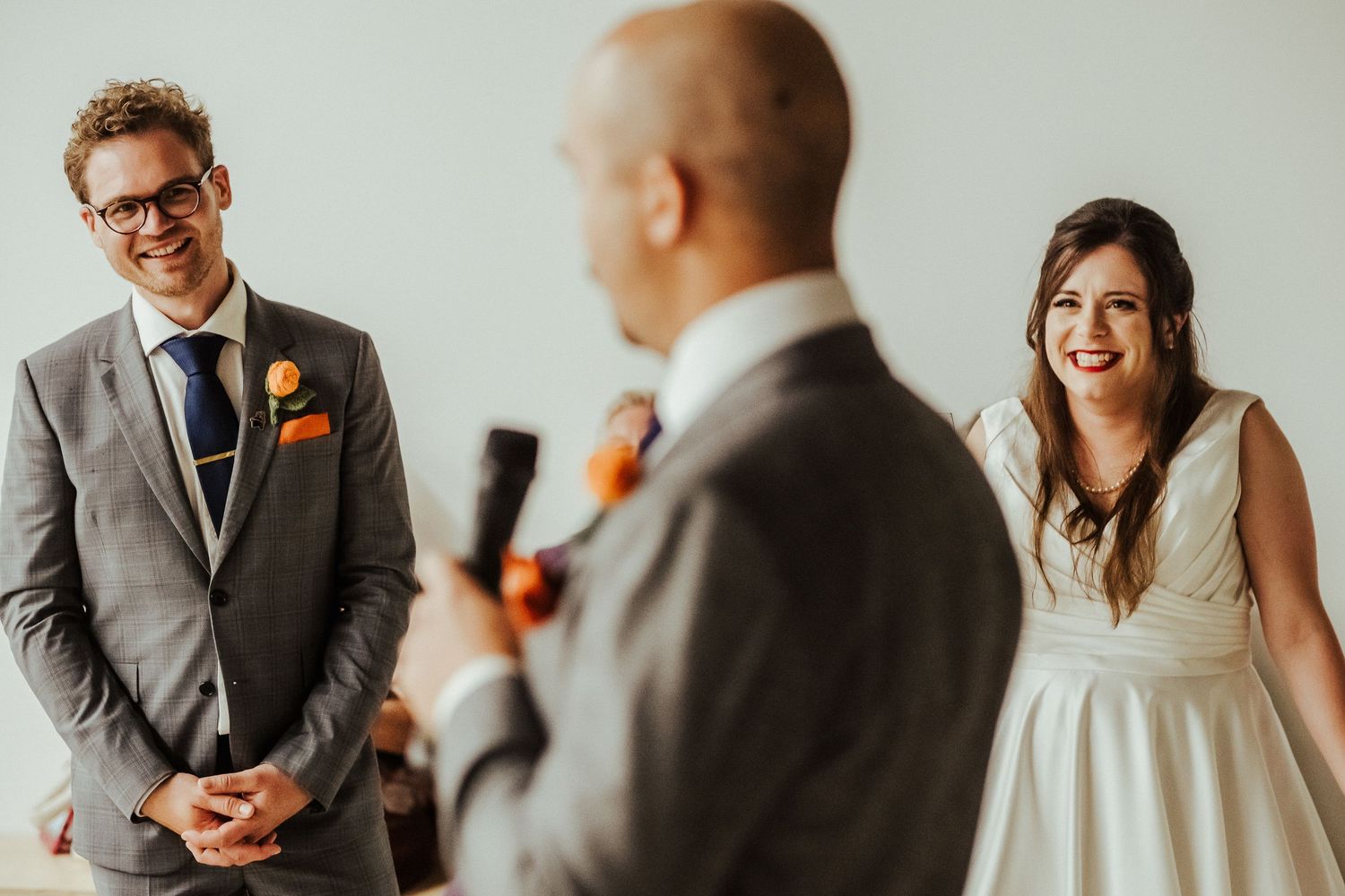 Wedding guests share joyful laughter during a ceremony speech by an officiant.
