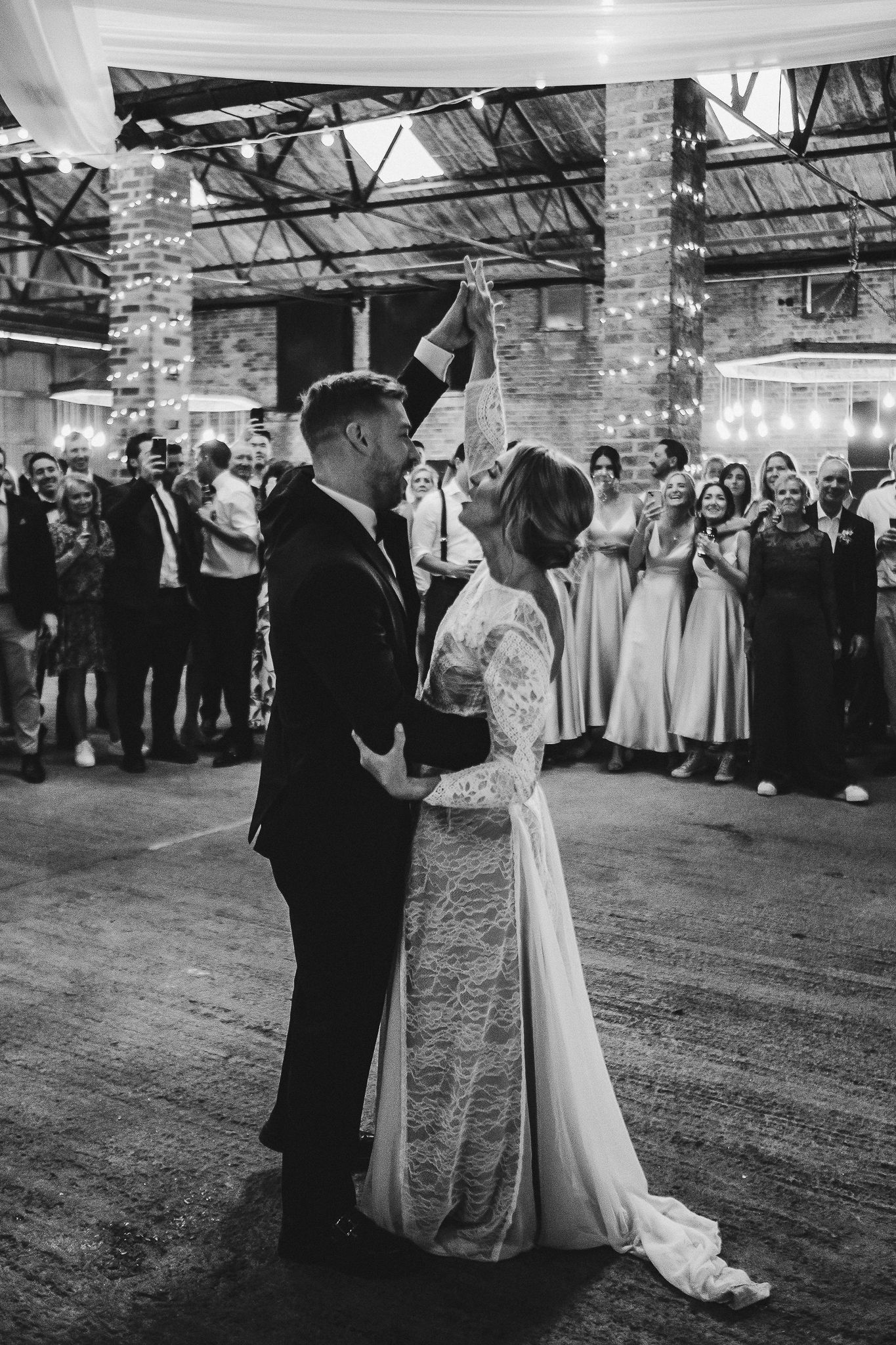A first dance between newlyweds in an industrial brick venue surrounded by wedding guests.